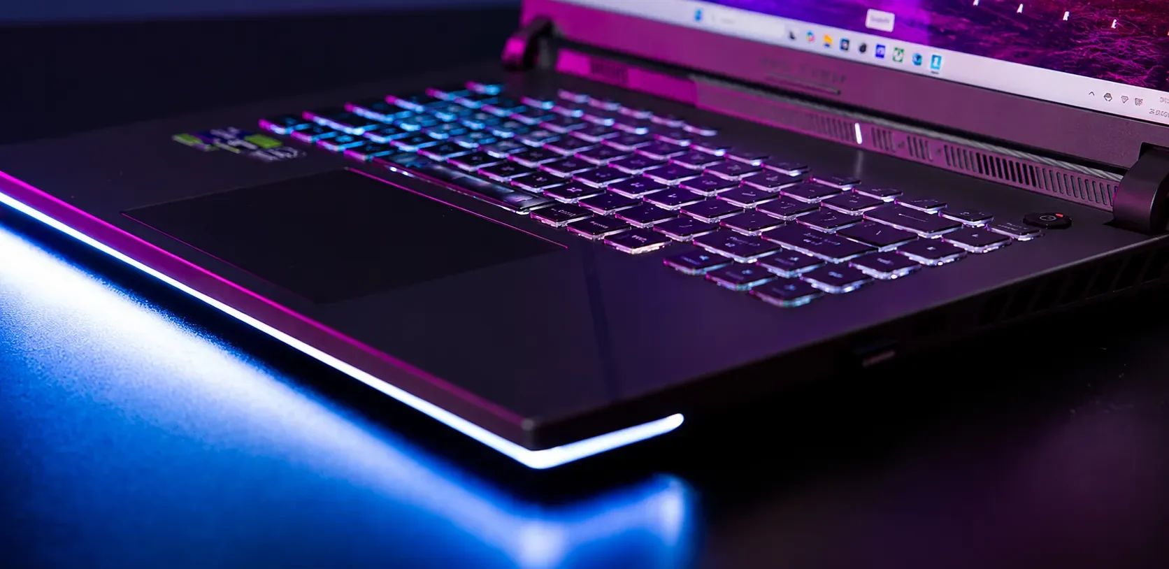 Close-up view of ASUS ROG Strix G16 RGB keyboard and chassis lighting illuminating a gaming desk